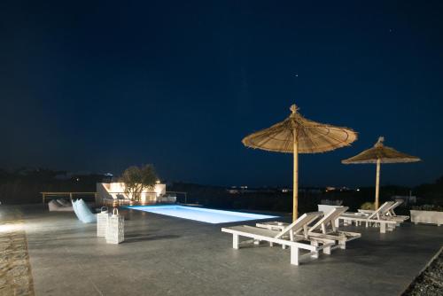 a pool with two umbrellas and chairs and a swimming pool at Andria's suites in Chrissi Akti