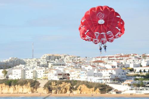 a red parachute is flying over a beach at AlbufeiraSun, arrive as a guest leave as a friend. in Albufeira