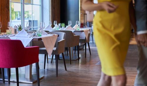 a woman in a yellow dress walks past tables with wine glasses at Hotel Residenz Hochalm - Joker Card Partner in Saalbach Hinterglemm