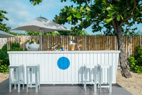 a bar with three chairs and an umbrella at JOIA Rose Hall by Iberostar - Adults Only All Inclusive Resort in Montego Bay