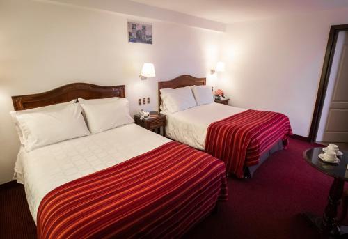 a hotel room with two beds with red and white sheets at Hotel Hacienda Plaza de Armas in Puno
