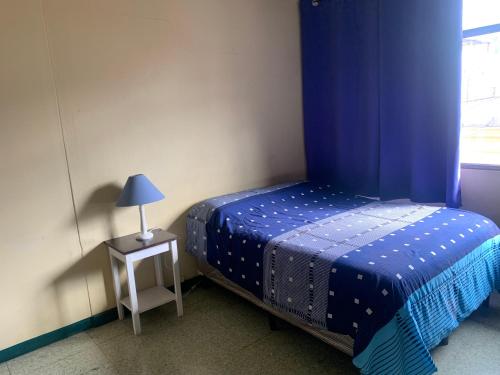 a bedroom with a blue bed and a table with a lamp at Kasa Kiwi Hostel & Travel Agency in Quetzaltenango