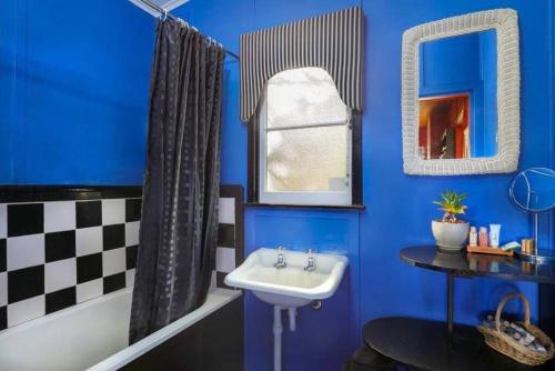 a bathroom with blue walls and a sink and a tub at Cherry Tree Cottage in Leura