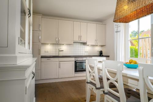a kitchen with white cabinets and a table with chairs at Ferien-im-Duenenhaus Lasse in Glowe