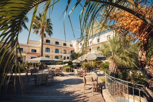 un patio con tavoli e sedie di fronte a un edificio di Hôtel Le Catalogne a Saint-Aygulf