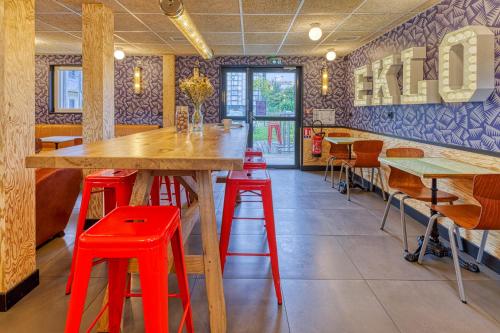 a restaurant with red stools and a large wooden table at Eklo Hotels Le Havre in Le Havre