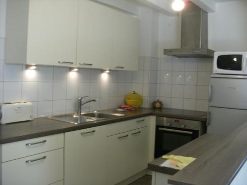 Una cocina con gabinetes blancos, un fregadero y un microondas. en Gite Des Alisiers, en Wattwiller