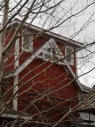 a red house with a white window and a tree at Au Cachalot Caché le gîte hôtel in Tadoussac