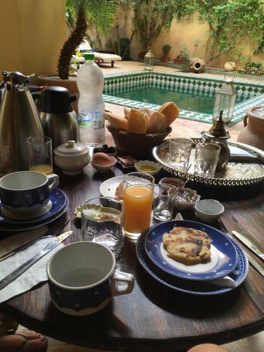a table with breakfast food and drinks and a swimming pool at Riad Dar Pierre in Fès