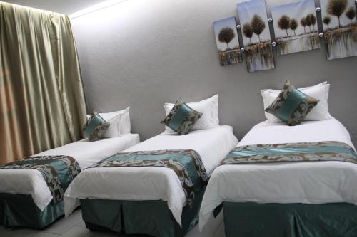 three beds in a room with white and green pillows at Urban Bliss Hotel in Kabwe