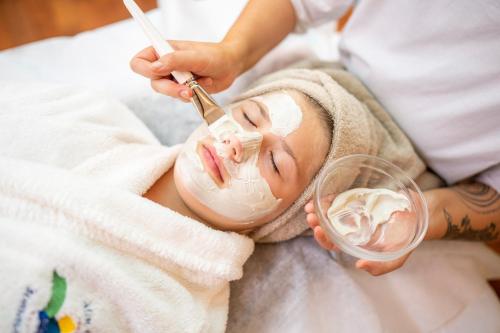a woman laying on a bed with a mask on her face with a glass at Familien- Sportresort BRENNSEEHOF in Feld am See