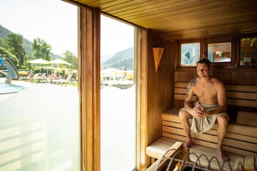 a man sitting in a sauna next to a swimming pool at Familien- Sportresort BRENNSEEHOF in Feld am See