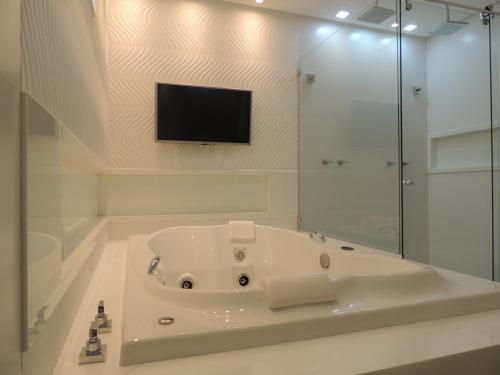 a white bathroom with a tub and a tv at Star Hotel in Itaperuna