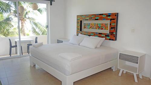 Un dormitorio con una cama blanca y una ventana grande. en El Fuerte Beach Apartments, en Mahahual
