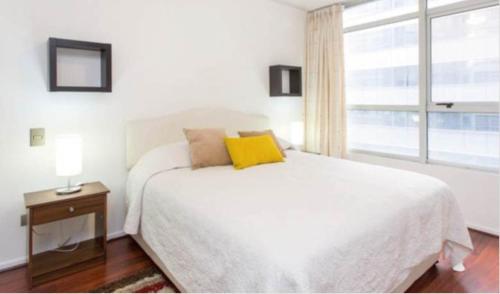 a white bedroom with a large bed and a window at SyS Suites Nueva San Martin in Santiago