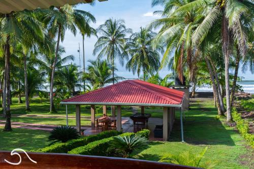 a pavilion with a red roof in a park with palm trees at Tranquilidad Resort in Parrita