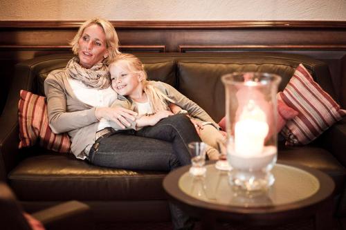 a woman sitting on a couch with a little girl at Hotel Strandhof in Baltrum