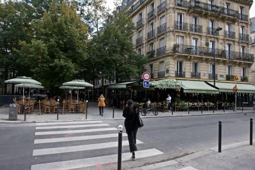 a woman walking across a crosswalk on a city street at CHARMING Parisian Apartment WITH AIR CONDITIONING - CLIMATISATION & 2 BEDROOMS - Batignolles PARIS in Paris