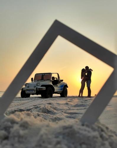a couple standing in front of a truck in the sand at Serra Mar Suítes,Lofts, e casas à 300 metros das praias in Arraial do Cabo
