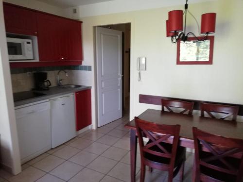 uma cozinha com armários vermelhos, uma mesa e cadeiras em Appart-dans Résidence de vacances au coeur du Golf-Le domaine de Gascogne em Biscarrosse