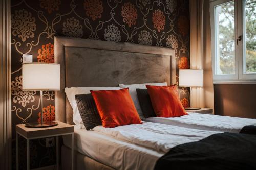 a bedroom with a bed with red pillows and two lamps at Hotel Dębowy Biowellness & SPA Góry Sowie in Bielawa