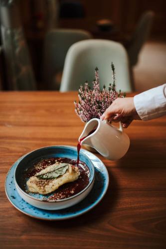 a person pouring sauce onto a plate of food at Hotel Dębowy Biowellness & SPA Góry Sowie in Bielawa