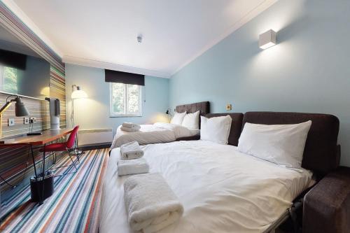 a large white bed in a room with a desk at Village Hotel Leeds North in Leeds