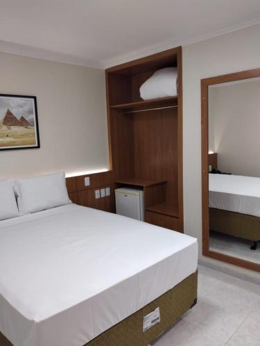 a bedroom with a large white bed and a mirror at Collina Hotel in Camapuã