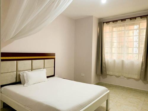 a bedroom with a white bed and a window at Easy Jkia Homestay in Nairobi