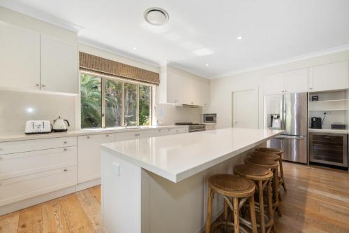 a kitchen with white cabinets and a large island with stools at Sandalwood in Avoca Beach
