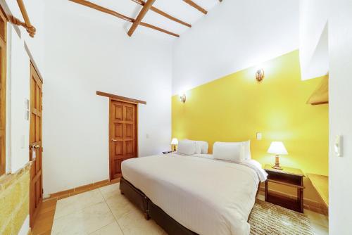 a bedroom with a white bed and a yellow wall at Hotel Jardines De La Villa in Villa de Leyva