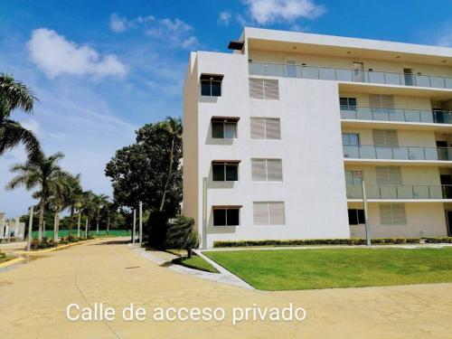 a white building with a palm tree in front of it at Departamento en condominio Diamante Turquesa in Acapulco