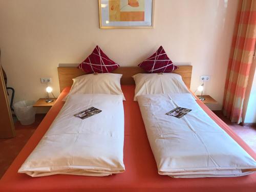 a bedroom with two beds with white sheets and red pillows at Pension & Café Meine Sonne Sole Mio in Bad Sooden-Allendorf
