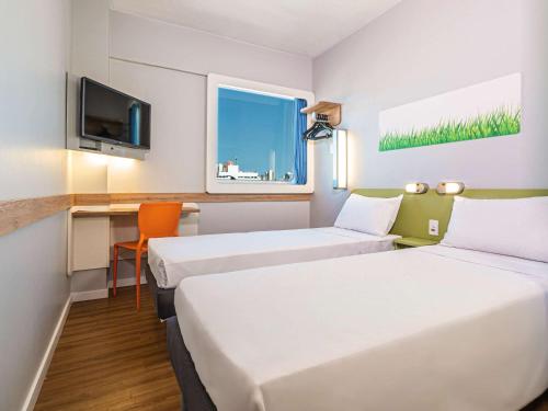 a room with two beds and a desk with a tv at Ibis Budget Fortaleza Praia de Iracema in Fortaleza