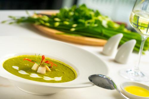Een kom groene soep op tafel met een glas wijn. bij Blanc Smith Residence in Siem Reap