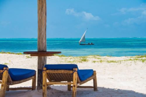 a beach with two chairs and a sail boat in the ocean at Amani Boutique Hotel - Small Luxury Hotels of the World in Paje
