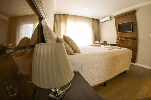 a bedroom with a bed with a lamp and a television at Hotel Gramado Interlaken in Gramado
