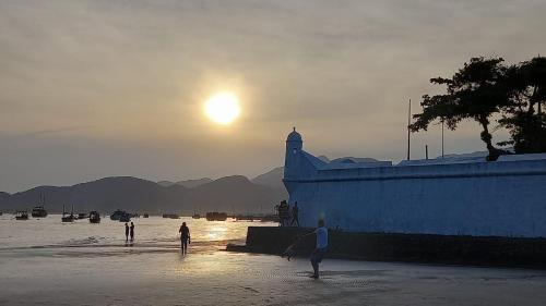 a group of people walking on the beach at sunset at BERTIOGA suítes na praia centro in Bertioga