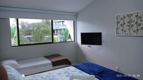 a bedroom with a bed and a tv and a window at Nannai Residence Porto Galinhas Praia Muro Alto 101 in Porto De Galinhas