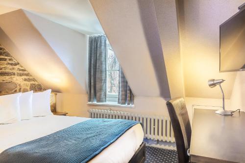 a bedroom with a bed and a desk and a window at Hotel Louisbourg in Quebec City