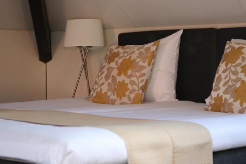 a bed with brown and white pillows and a lamp at Hotel Hof van 's Gravenmoer in 's-Gravenmoer