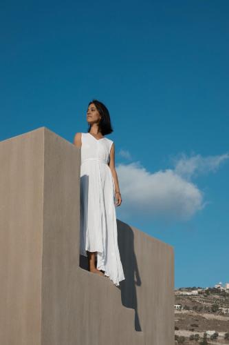 a woman in a white dress standing on a wall at Santorini Sky, The Lodge in Pirgos