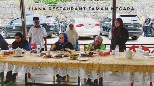 um grupo de pessoas sentadas à volta de uma mesa com comida em Liana Hostel Taman Negara em Jerantut