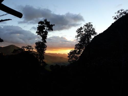 a sunset in the mountains with trees in the foreground at Chales Bamboo Jungle in Petrópolis