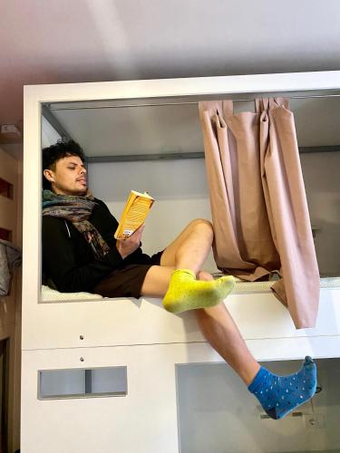 a man sitting on a shelf reading a book at Good People Design Hostel in Belgrade