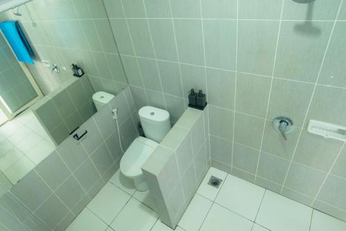 a white tiled bathroom with a toilet and a shower at Mad Monkey Kuta Lombok in Kuta Lombok
