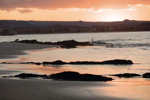 a sunset on the beach with rocks in the water at X Kirra Apartments in Gold Coast
