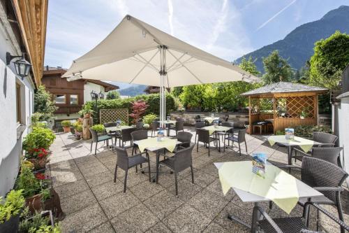 a patio with tables and chairs and an umbrella at Hotel Neuwirt in Finkenberg