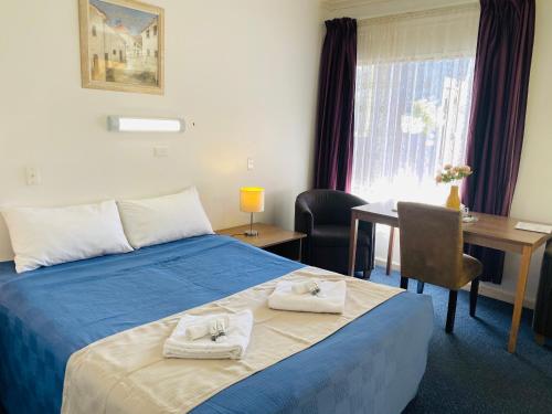 
a hotel room with a bed, desk, chair, and nightstand at Barossa Gateway Motel in Nuriootpa
