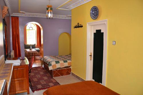 a bedroom with yellow walls and a bed and a window at Ksar Timnay Hotel in Aguelmous